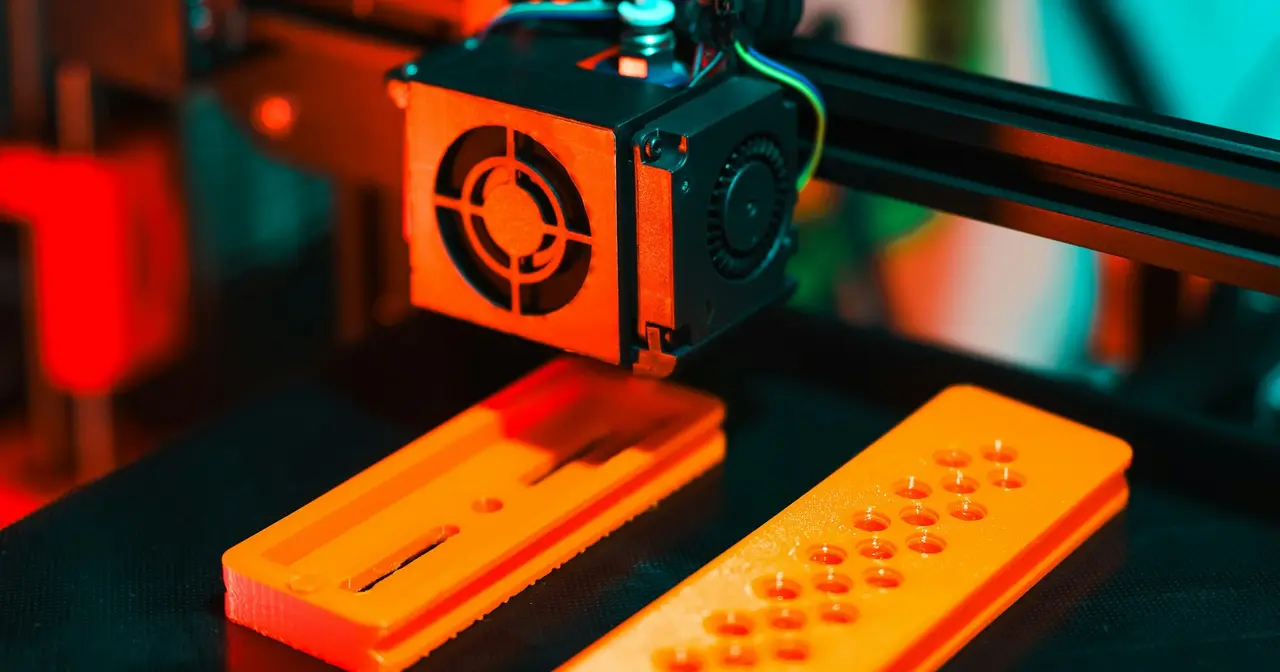 3D-принтер печатает оранжевые пластиковые детали